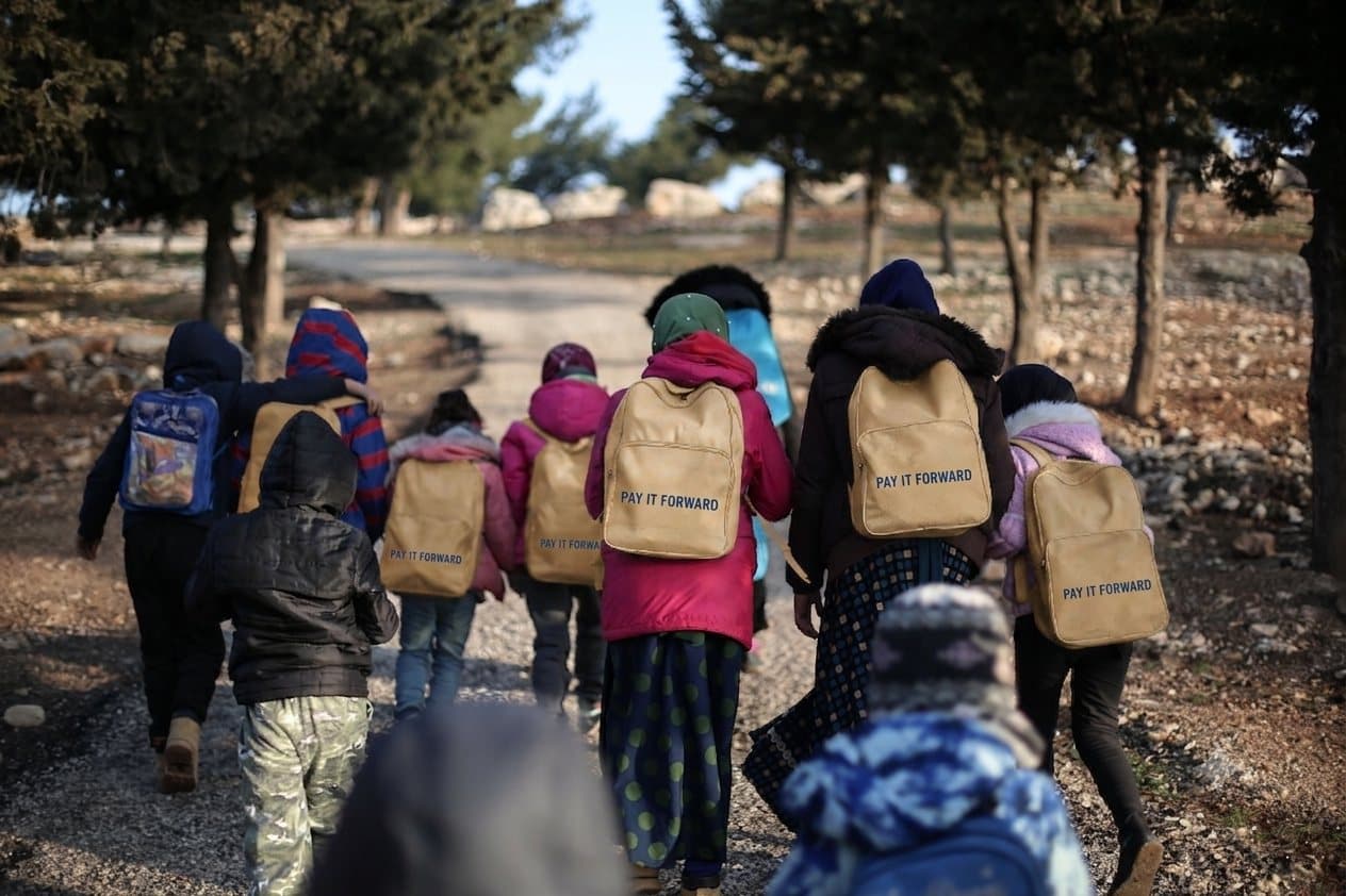 Niños caminando con mochilas de Pay it forward